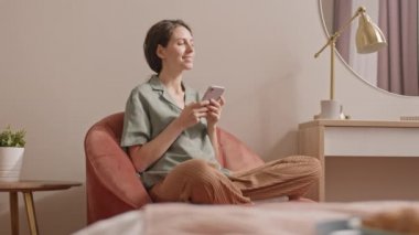 Kafkasyalı mutlu bir kadın, şezlongda oturuyor, ayakları koltukta oturuyor, cep telefonundan arıyor, gülümsüyor ve konuşuyor.