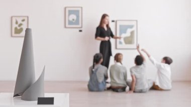 Sanat eserlerinden müzenin zemininde oturan çocuklara odaklanmak, beyaz kadının duvardaki resimler hakkında konuşmasını dinlemek.