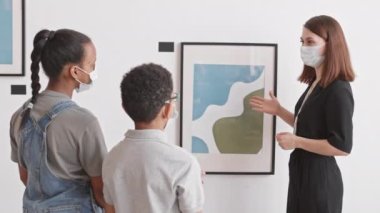 Sanat galerisi çalışanlarını izleyen iki Afrikalı ortaokul öğrencisinin duvar resimleri hakkında sunum yaptığı, hepsinin yüz maskesi taktığı bir ortam.