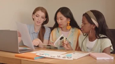 Üç genç, çok ırklı moda tasarımcısının belden yukarısı çizimleri tartışıyor.