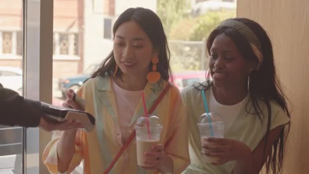 女性の友人とカフェに座っているクレジットカードでアイスコーヒーを支払う幸せな若いアジアの女性のウエストアップショット — ストック動画