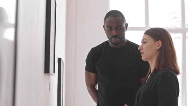 背景照片 年轻的白人女人和身穿黑色衣服的非洲男人站在艺术画廊 讨论墙上看不见的画 — 图库视频影像
