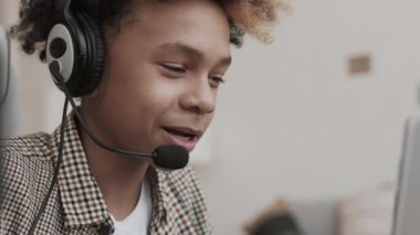 Genç Afrikalı bir çocuğun mikrofonla arkadaşlarıyla internet üzerinden iletişim kurup içeride oturması.