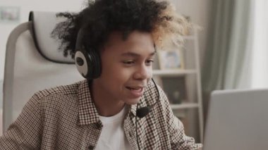 Kulaklık takan enerjik Afrikalı bir gencin göğüsleri, odasında masasında oturuyor, mikrofonla konuşuyor ve online oyunda başarısız oluyor.