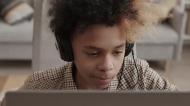 13 yaşında, mikrofonlu kulaklık takan, odasında oturmuş arkadaşlarıyla internetten video oyunu oynayan bir çocuğun yüksek açılı yakın çekimi.