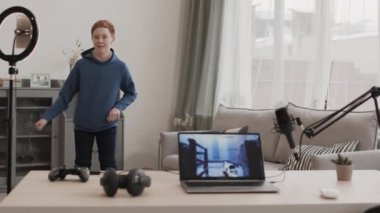 Orta uzunlukta, mavi kapüşonlu, dans eden ve gülümseyen beyaz bir çocuk sosyal ağ sitesinde kısa format videosu kaydederken, bilgisayarda aralıklı video oyunu oynuyordu.