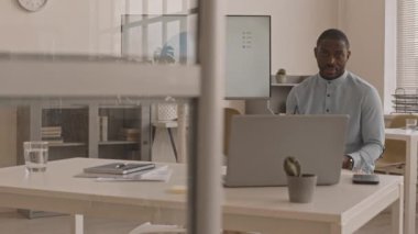 Gündüz vakti resmi olarak masa başında oturan, dizüstü bilgisayarla video konferansı yapan, sunum yapan, konuşan Afrikalı erkek ofis çalışanlarının tam ortasını izlemek.
