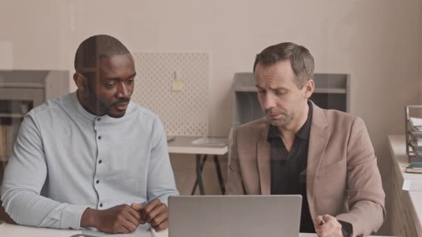 Orta yaşlı, beyaz ve genç Afrikalı erkeklerin belden yumağı ofiste oturuyor, bilgisayarla çalışıyor, sohbet ediyorlar.