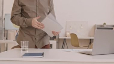 Beyaz erkek katibin, masasına dokümanları taşırken, sandalyeye otururken, taşınabilir bilgisayar üzerinde çalışmaya başlarken...