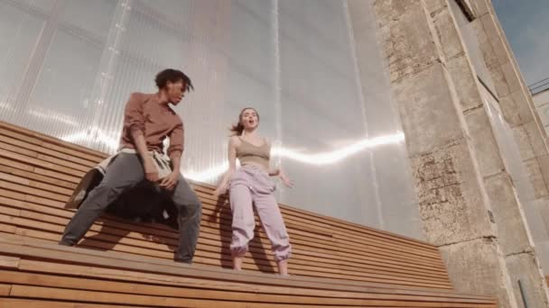在温暖的夏日里 两个不同的年轻舞者在户外木制长椅上表演着各种各样的舞步 他们的角度很低 — 图库视频影像
