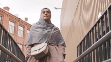 Düşük açılı, kendine güvenen, tesettürlü ve bel çantalı genç bir Arap kadının şehirde tek başına yürürken çekilmiş yavaş çekimleri.