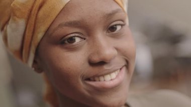 Kafasında sarı sarılık olan, arka planda kameraya gülümseyen Afrikalı Amerikalı genç bir kadının yakın plan portresi.