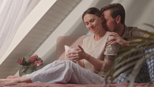 年轻可爱的白人异性恋夫妇坐在床上 女人笑着 早上喝一杯咖啡 — 图库视频影像