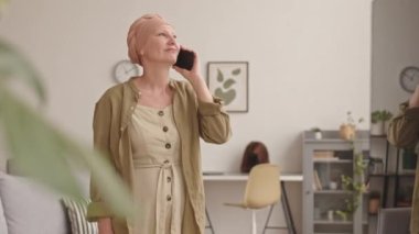 Orta yaşlı, başörtüsü takan, telefonla konuşan ve kanser gerilemesini kutlamak için dans eden bir kadının orta boy fotoğrafı.