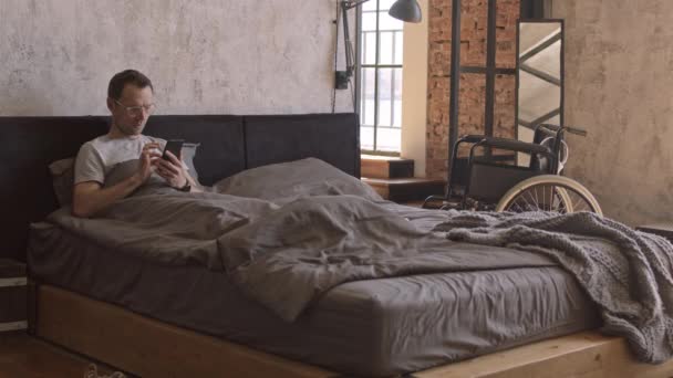 Szeroki Mężczyzna Rasy Kaukaskiej Leżący Łóżku Korzystający Smartfona Wózek Inwalidzki — Wideo stockowe