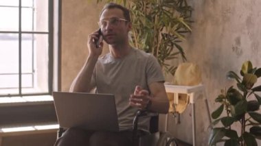 Tekerlekli sandalyede oturan, dizüstü bilgisayar ve akıllı telefon kullanarak çalışan beyaz bir adama tahta oyuncakları yere yatırmak.