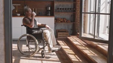 Barışçıl, tekerlekli sandalyedeki kadın sabahları mutfaktan kahve içiyor, pencereden içeri bakıyor.