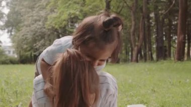 Medium shot of cute playful toddler boy having fun with mom lying on grass in park on warm sunny day
