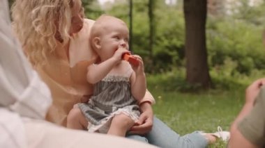 Medium close-up of two cute toddler boy and girl playing with moms outdoors sitting on green grass in summer