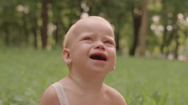 Medium close-up of little girl in summer dress crying outdoors in park