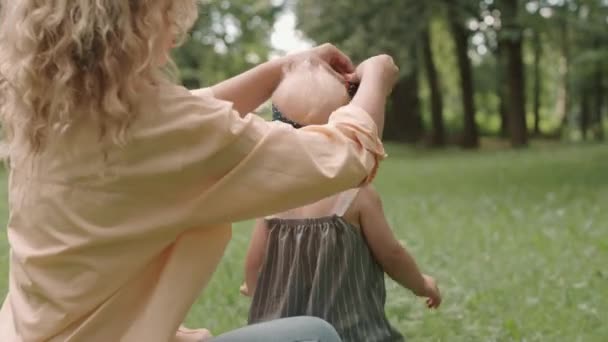 年轻女子在公园休息和度过夏天时 在她漂亮的小女儿头上涂上波尔卡圆点蝴蝶结的中景照片 — 图库视频影像