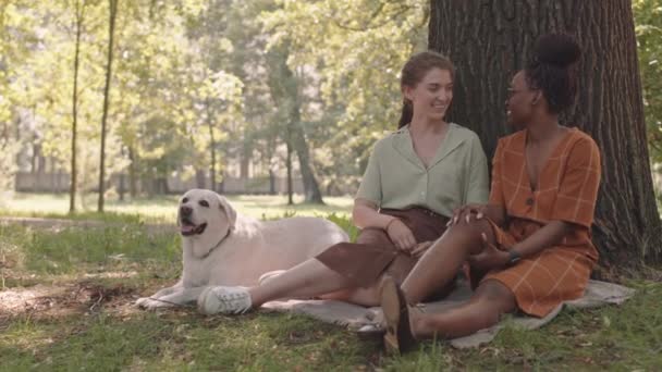 Wide Shot Two Young Diverse Girlfriends Dog Sitting Grass Leaning — Αρχείο Βίντεο