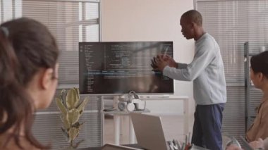 Orta uzunluktaki heyecanlı Afrikalı bilişim uzmanı sunum yapıyor, ekranda tanınmayan yatırımcılara bilgisayar kodlarını gösteriyor