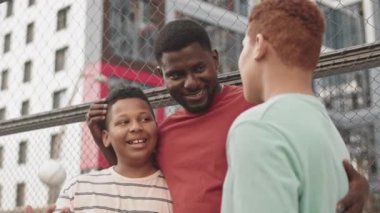 Afrika kökenli Amerikalı bir baba ve iki genç oğlunun spor sahasında sohbet ederken çekilmiş bir fotoğrafı.