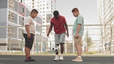 Afrikalı Amerikalı bir adam ve iki genç oğlunun spor sahasında futbol antrenmanı yaparken, iki ayakla zıplayan bir futbol sahnesi.