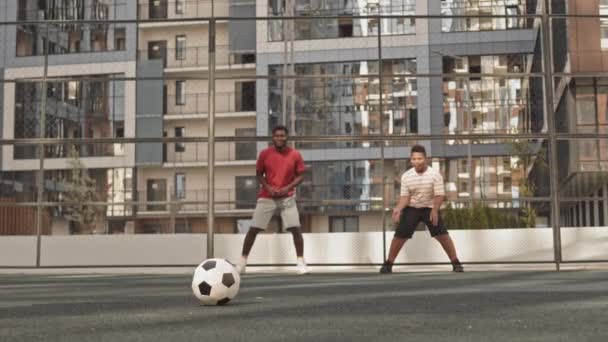 美国黑人男子和他的两个十几岁的儿子在户外有栅栏的运动场上踢足球的慢镜头 — 图库视频影像