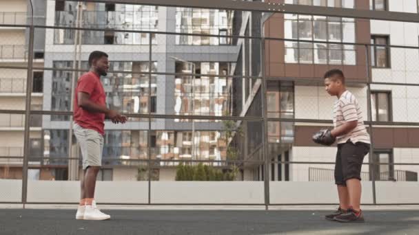 美国黑人男子教他十几岁的儿子打棒球 站在运动场前面 投球和接球的侧面全景镜头 — 图库视频影像
