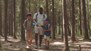 Afrika kökenli Amerikalı bir adamın, oğullarıyla birlikte güzel yaz ormanlarında birlikte kamp yaparken sırt çantalarını taşırkenki yavaş çekimleri.