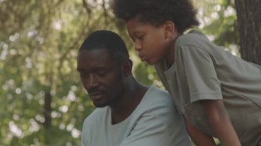 Afrika kökenli Amerikalı bir adam ve küçük oğlunun ormanda balık tutarken güneşli havanın tadını çıkarırken çekilmiş orta boy bir fotoğrafı.