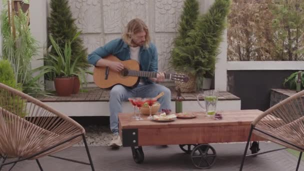 Junger Langhaariger Hipster Mann Jeans Spielt Akustikgitarre Und Sitzt Auf — Stockvideo