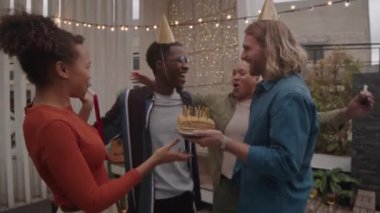 Doğum günü pastasında mumları üfleyen neşeli Afro-Amerikalı genç adam ve bir grup arkadaşı yaz akşamları çatıda ip ışıklarıyla birlikte zum yapıyor.