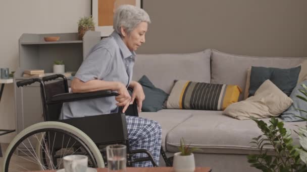 穿着休闲服 中等身材 头发灰白的亚洲女人下了轮椅 坐在家里的沙发上 — 图库视频影像