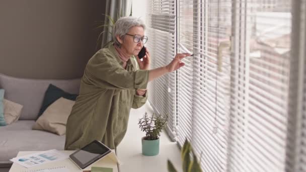 亚洲现代女性中年人站在窗边 用手机交谈 透过百叶窗偷窥 — 图库视频影像