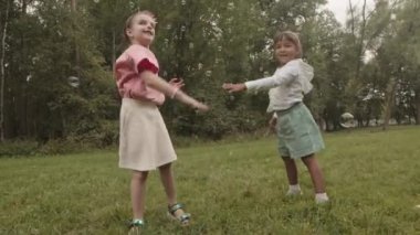 Düşük açı, beş yaşında gülümseyen, dans eden ve çimenlikteki yaz parkında sabun köpüğü yakalayan iki çoklu etnik kızla dolu.