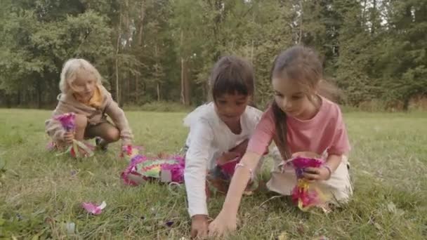 緑の公園で壊れたピナタから落ちたキャンディーを拾う多様な小学校の幅広いショット — ストック動画