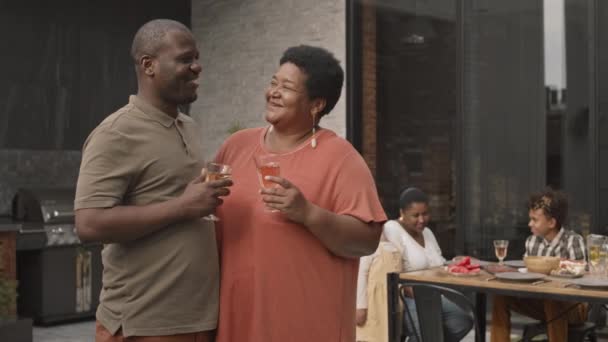 成熟したアフリカの女性と彼女の大人の息子のグラスからワインを飲んで 話して 家族の前でテラスに立って食事 — ストック動画