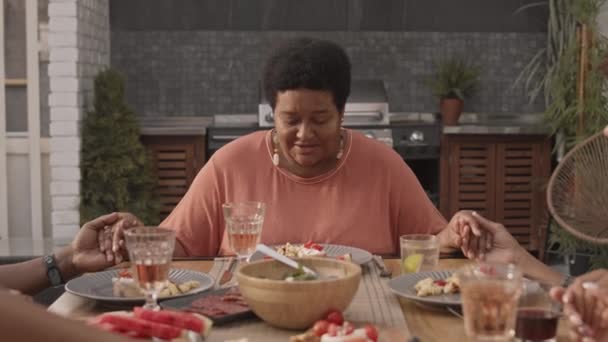 成熟的非洲裔美国妇女坐在餐桌前 与收割的家人手牵手 在晚饭前祈祷 她们的胸部鼓起了勇气 — 图库视频影像
