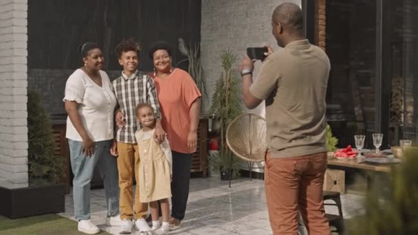 Młody Afrykanin Pomocą Smartfona Robienia Zdjęć Swojej Rodzinie Pozowanie Podwórku — Wideo stockowe