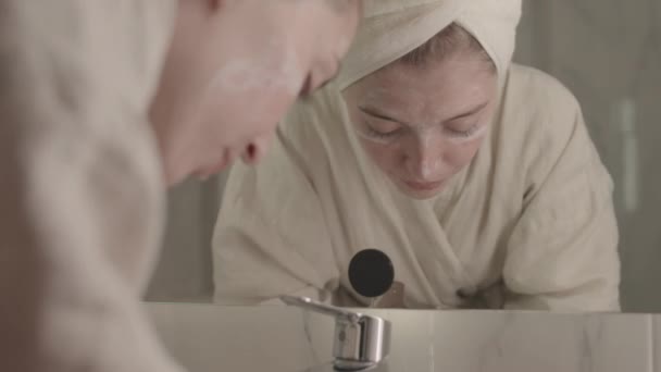 白种人年轻女子站在大理石浴室镜子前 用水洗去面罩的倾斜镜头 — 图库视频影像