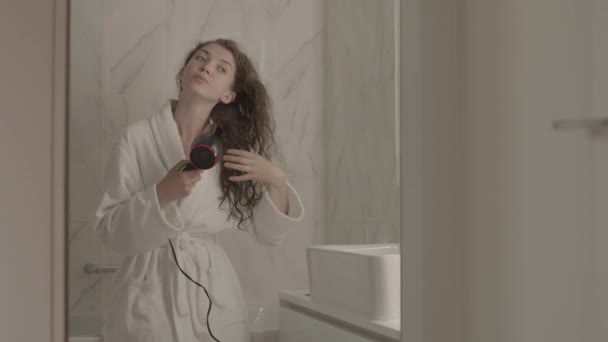 Beyaz Bornozlu Uzun Kıvırcık Saçlarını Kurutan Mermer Banyoda Aynanın Önünde — Stok video