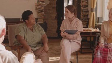 Huzurevinde daireler çizen bir grup yaşlıyla konuşurken genç bir kadının not aldığı yavaş çekim.