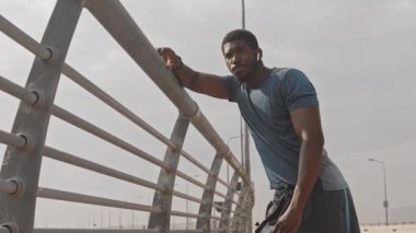 Düşük açılı yavaş çekim, yorgun Afrika kökenli Amerikalı erkek sporcunun koşudan sonra dinlenmesi ya da yarış pistinde koşması, su içmesi ve kablosuz kulaklıkla müzik dinlemesi.