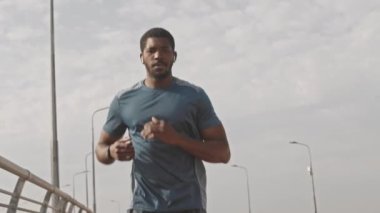 Afrika kökenli genç erkek sporcu, yaz sabahı yarış pisti boyunca koşuyor, akıllı adımlara bakıyor ve dinlenmek için mola veriyor.