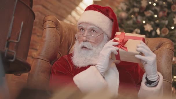 Noel Baba Nın Evdeki Koltukta Oturup Küçük Hediye Kutusunu Sallarken — Stok video