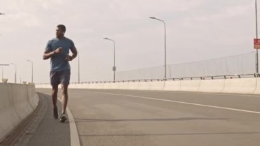 Güneşli bir sabahta boş yolda koşan spor giysili Afro-Amerikalı genç bir adamın uzun ve yavaş yürüyüşü.