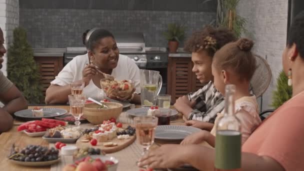 年轻的黑人妇女坐在阳台上的餐桌旁 向家人提供沙拉 并为家人提供沙拉 — 图库视频影像
